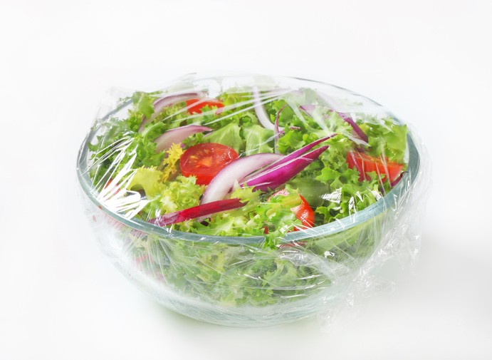 Salada de legumes em uma tigela de vidro coberta com filme plástico.